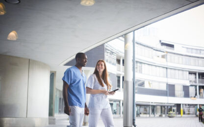 Confident nurses discussing while walking on footpath at hospital seen through glass